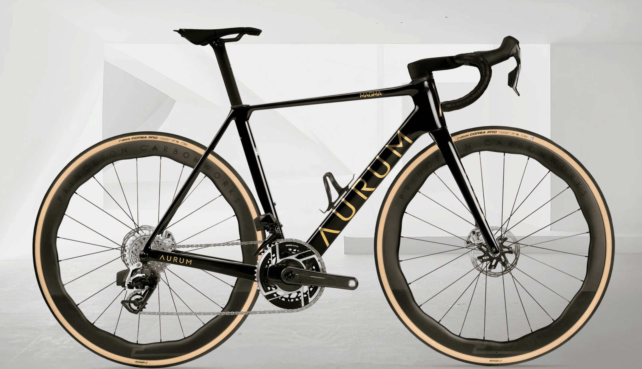 Sort AURUM Magma landeveissykkel med gull detaljer og Princeton-hjul, fotografert fra siden mot en lys, minimalistisk bakgrunn.