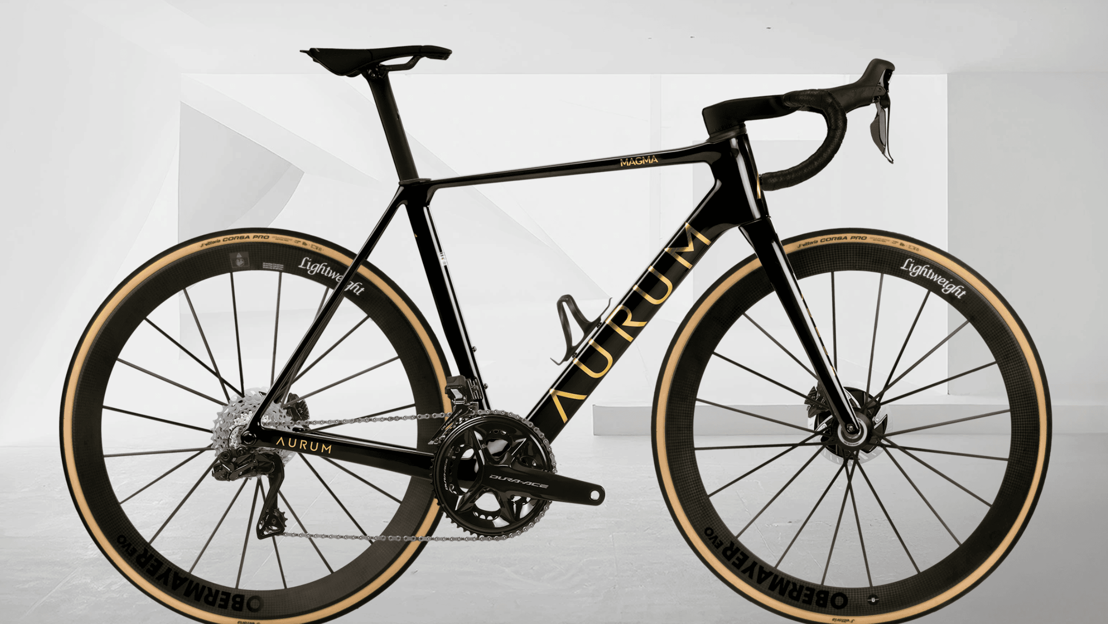 Sort AURUM Magma landeveissykkel med gullfargede detaljer og Lightweight-hjul, fotografert fra siden mot en lys, minimalistisk hvit bakgrunn.