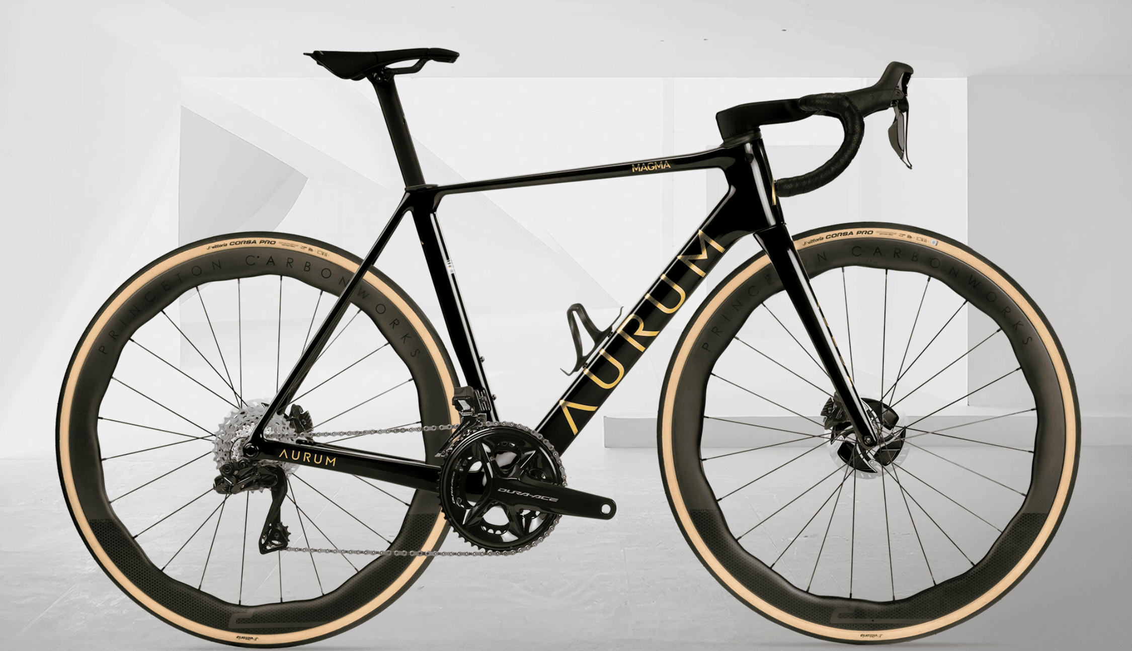 Sort AURUM Magma landeveissykkel i karbonfinish med gull detaljer og Princeton-hjul, fotografert fra siden mot en lys, minimalistisk bakgrunn.