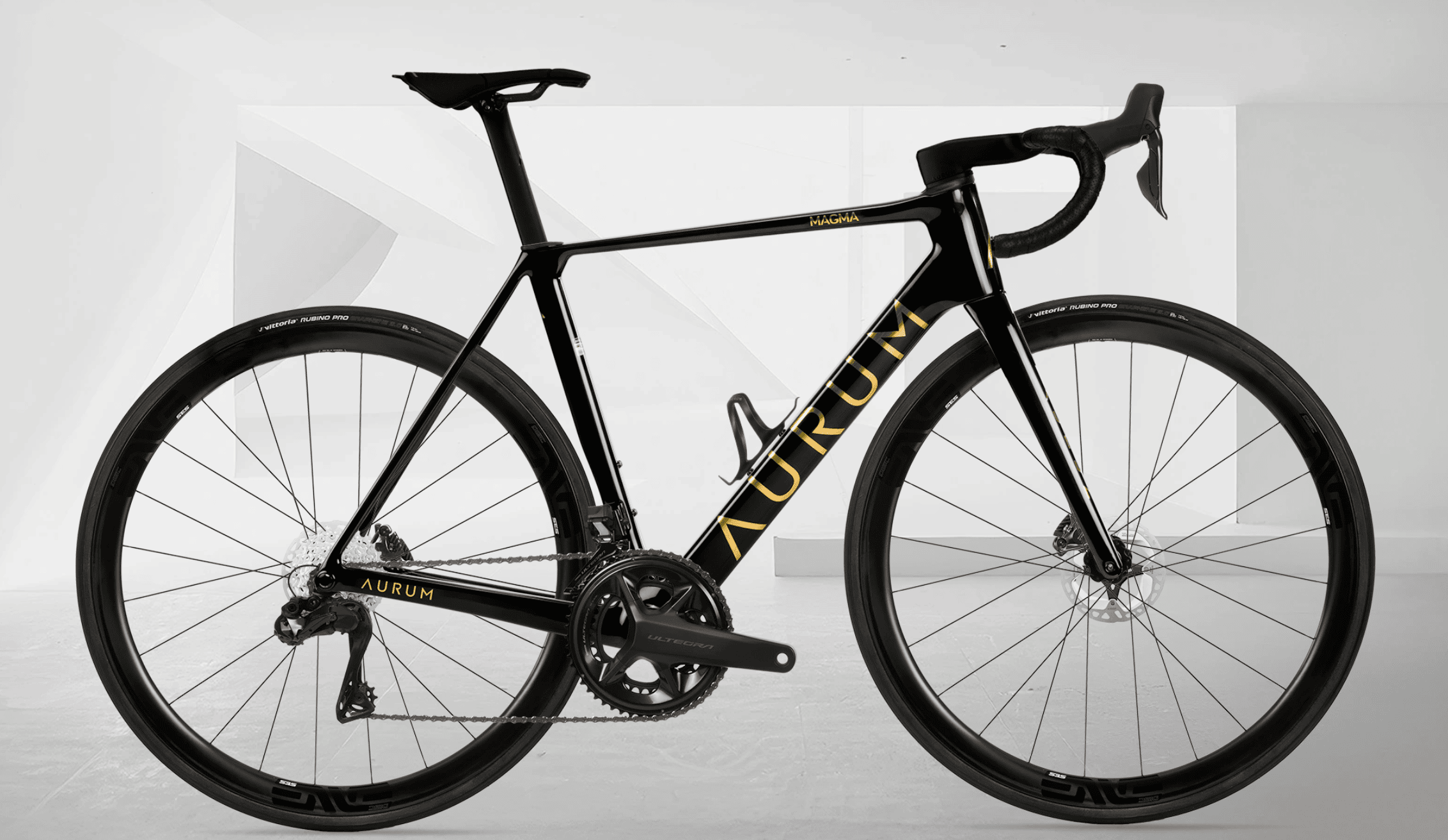 Sort AURUM Magma landeveissykkel med gullfargede detaljer, sett fra siden mot en lys og minimalistisk hvit bakgrunn.